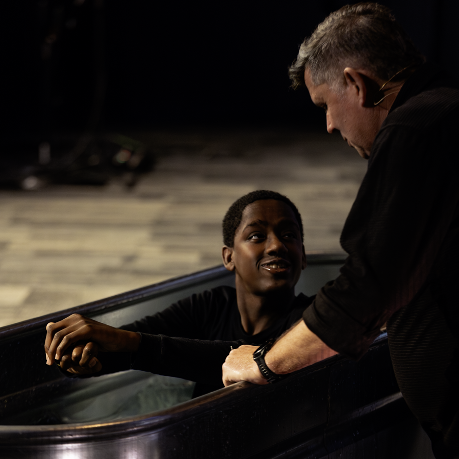 a young man smiles up at his pastor from the baptismal tub
