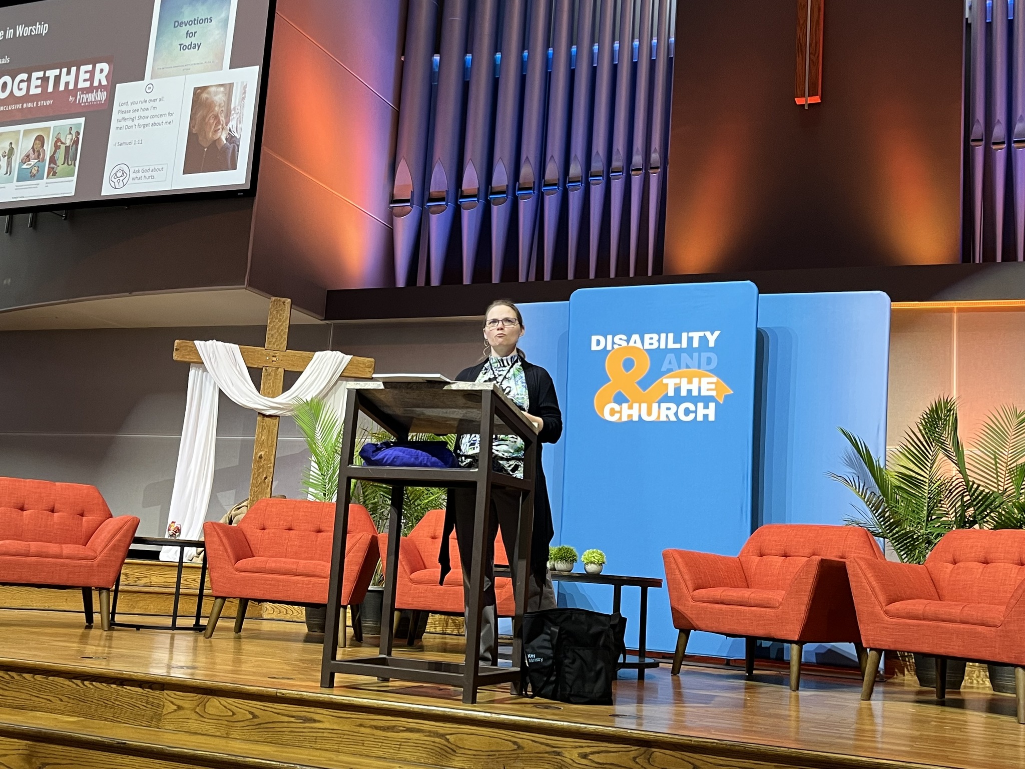 a middle aged woman standing at a podium with a cross in the background as well as a banner that says 